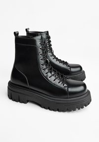 Černé kotníkové kožené boty s hladkým povrchem, kulatou špičkou a silnou, texturovanou gumovou podrážkou. Mají kovové očka a tkaničky.