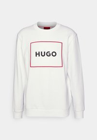 Sudadera blanca de manga larga, con un diseño rectangular bordeado en rojo y la palabra "HUGO" en letras negras negritas. Textura de tejido suave.