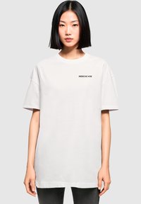 Hvid oversized t-shirt lavet af bomuld med korte ærmer. Har et sort "MERCHC•DE" logo på venstre brystområde.