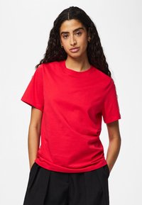 Rød bomuldst-shirt med korte ærmer og rund halsudskæring, med en glat tekstur og afslappet pasform, kombineret med sorte bukser.