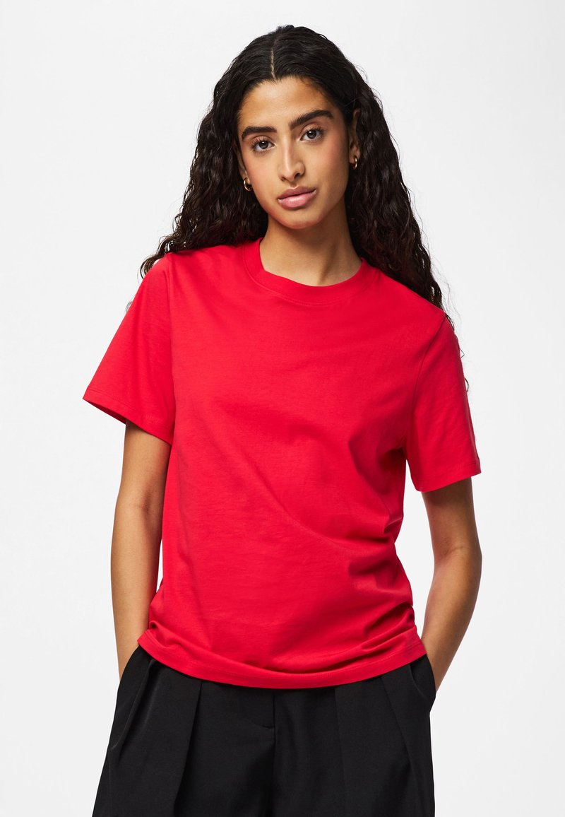 Rød bomuldst-shirt med korte ærmer og rund halsudskæring, med en glat tekstur og afslappet pasform, kombineret med sorte bukser.