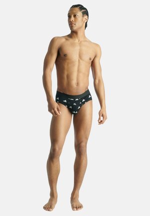 Schwarze Schwimmslips mit weißem geometrischem Muster. Hergestellt aus elastischem Material, mit breitem elastischem Bund und figurnaher Passform.
