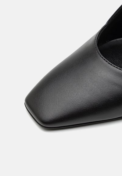 Zapato de cuero negro con punta afilada y textura suave. Tiene un diseño de corte bajo con un sencillo detalle de borde cosido.