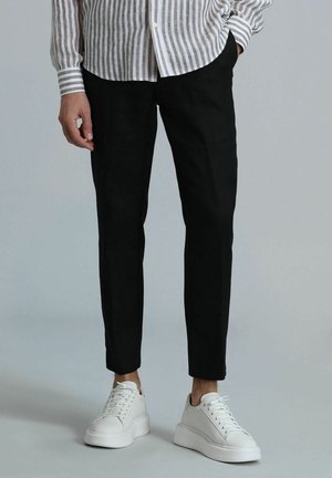 Zwarte tapered pants van lichtgewicht stof, gecombineerd met witte sneakers met een gladde afwerking en dikke zolen.