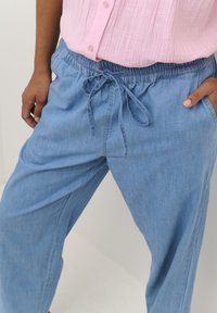 Ljust blå denimjoggingbyxor med elastisk midja, dragsko och sidofickor. Tyget har en mjuk, något strukturerad yta.