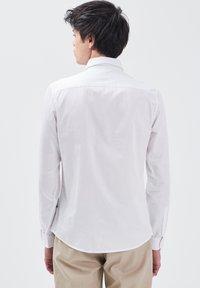 Witte langesleeve shirt met een kraag en knoopmanchetten, gemaakt van soepele stof. Ronde zoom aan de achterkant, minimalistisch ontwerp.