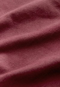Tissu bordeaux doux et froissé avec une texture fine en maille et des ombres subtiles mettant en valeur ses plis.