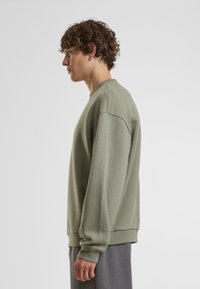 Olivengrøn sweatshirt med lange ærmer og ribbede manchetter. Har en rund halsudskæring og en afslappet pasform, lavet af blødt, struktureret stof.