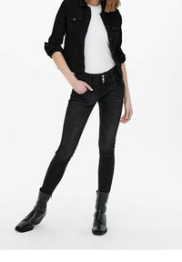 Svarta denimjeans med slim fit, med fem fickor, knappstängning och subtila blekningar. Kombinerat med en vit skjorta och svarta ankelboots.