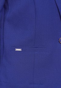 Niebieska marynarka z teksturowanej tkaniny, z jedną kieszenią ozdobioną srebrną metką oraz wyraźnym guzikiem na przodzie.