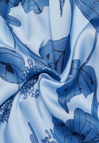 Tessuto di seta azzurro chiaro con un motivo floreale in tonalità blu scuro, dalla texture morbida e dal drappeggio fluido. Design dettagliati di foglie e petali.