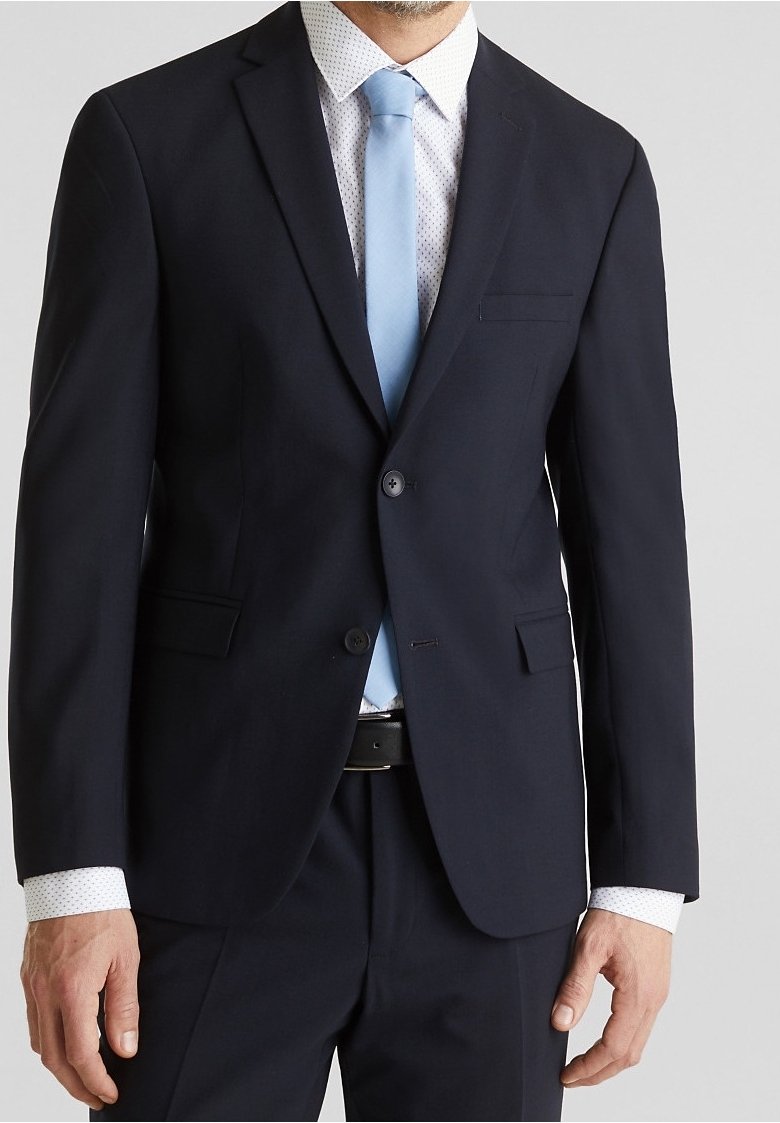 Giacca da abito blu navy con vestibilità slim, abbinata a una cravatta azzurro chiaro e una camicia bianca con piccoli punti blu. Colletto a punta, dettaglio con una tasca.