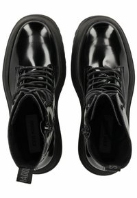 Botines de charol negro con un diseño de cordones, suelas de goma y cremalleras laterales. Presentan un acabado suave y brillante.