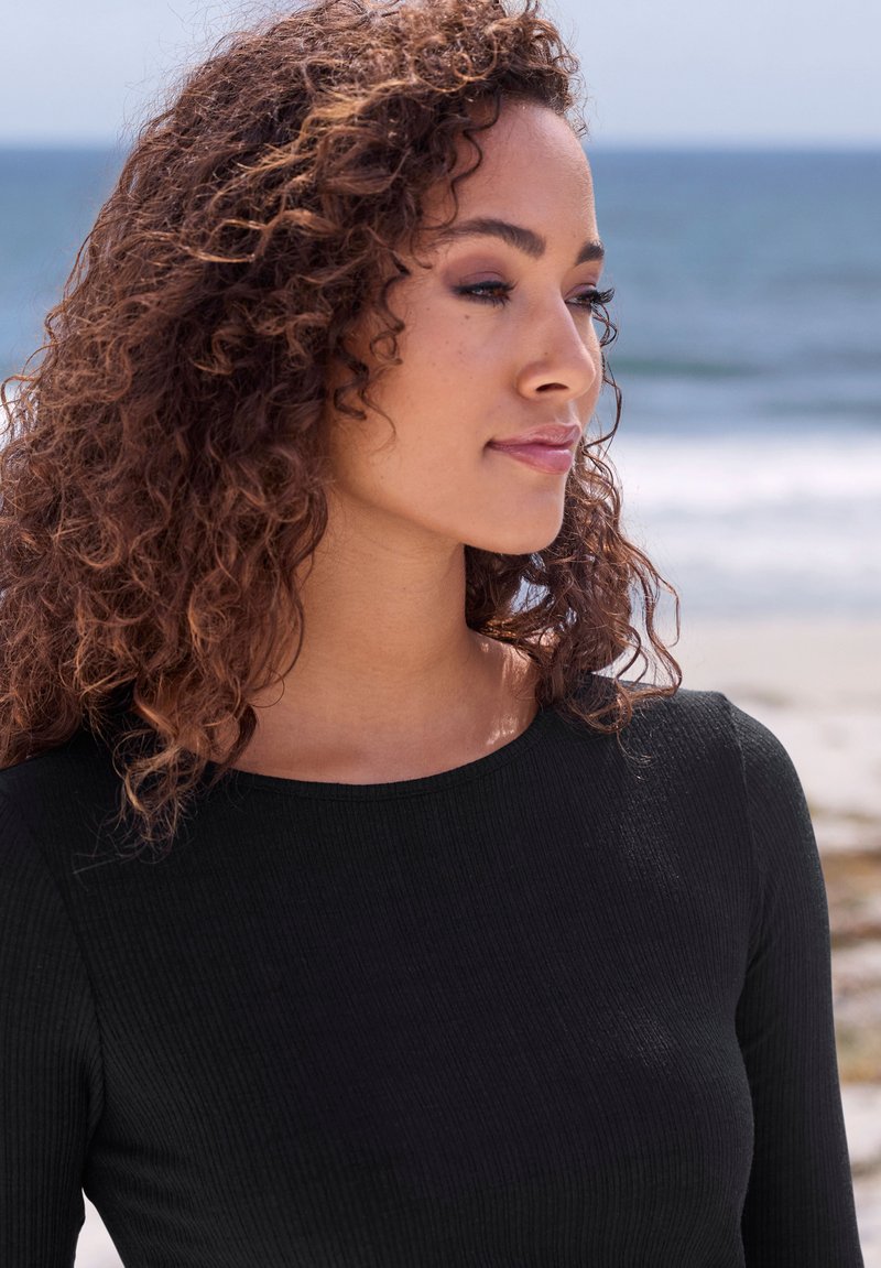 Musthave mustripi musta pikkade varrukatega särk, ümmarguse kaelusega. Subjektil on lokkis juuksed, taustal on rand koos pehme fookusega ookeaniga.