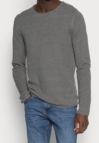 Maglietta grigia a maniche lunghe con un motivo a maglia texturizzato e scollatura rotonda, abbinata a jeans in denim blu.