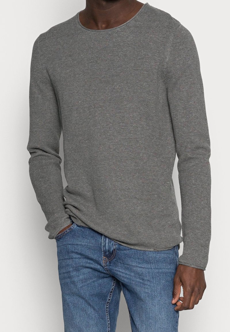 Maglietta grigia a maniche lunghe con un motivo a maglia texturizzato e scollatura rotonda, abbinata a jeans in denim blu.