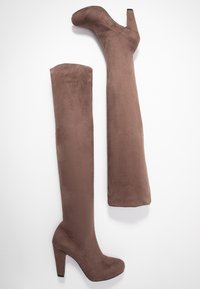 Botas marrones por encima de la rodilla con una textura suave similar al ante, tacón alto y punta redondeada, exhibidas una al lado de la otra sobre un fondo blanco.