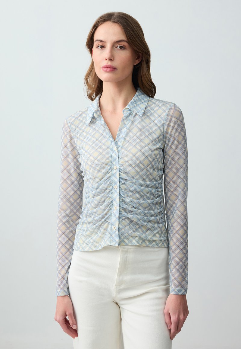 Blusa leggera e trasparente a maniche lunghe con un motivo a quadri blu e giallo, caratterizzata da una chiusura con bottoni frontale e dettagli arricciati lungo i lati.