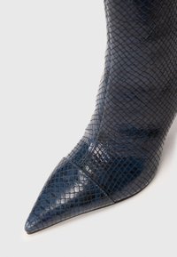 Botín de tacón alto en imitación de serpiente azul marino oscuro, con puntera afilada, superficie texturizada con un brillo sutil, que presenta un diseño de parte superior lisa.
