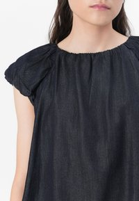 Mørk denim topp med sammenkrøllede ermer og elastisk halslinning. Stoffet har en subtil tekstur og en løs, flytende design.