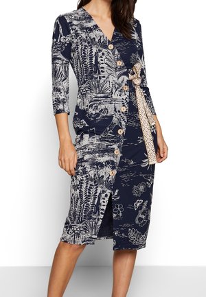 Granatowa sukienka kopertowa z beżowym botanicznym wzorem, drewnianymi guzikami z przodu, rękawami o długości do łokcia oraz wzorzystym beżowym paskiem do wiązania.