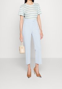 Raidallinen lyhythihainen paita vaaleansinisessä ja kermanvärisessä, räätälöidyt vaaleansiniset housut, beige käsilaukku ja teräväkärkiset ruskeat korkokengät.