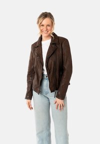Chaqueta de cuero marrón de motorista con estampado de leopardo, cierre con cremallera en la parte delantera, collar de solapa y acabado texturizado, combinada con jeans azul claro y una camisa blanca.