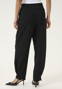 Pantalons larges noirs avec taille haute, deux poches arrière et design ajusté. Ajustés aux chevilles avec des détails en boutons.
