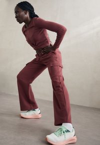 Top corto de color marrón rojizo de manga larga y pantalones cargo de cintura alta con bolsillos; combinado con zapatillas deportivas de color verde claro y negro.