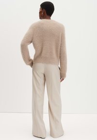 Pull en fausse fourrure beige clair à manches longues, col rond et coupe décontractée, associé à un pantalon crème taille haute à jambes larges.