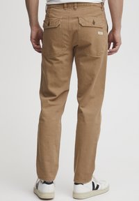 Tan cotton pants with a straight leg design, featuring two back pockets and a label, paired with white sneakers with black accents.