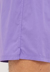 Μωβ μαγιό από ελαφρύ ύφασμα, με πλαϊνές σχισμές, καθαρά ραμμένα τελειώματα και απλό σχέδιο χωρίς μοτίβα ή διακοσμητικά στοιχεία.