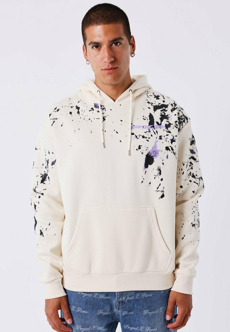 Crème hoodie met zwart en paarse spetterpatroon, capuchon met trekkoord, voorzak en ribgebreide manchetten. Zachte, katoenen stofmix.