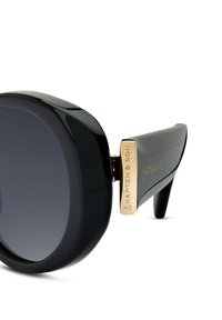 Černé oversized sluneční brýle vyrobené z lesklého plastu, s zlatým akcentem na stranu, na které je vygravírováno "KAPTEN & SON". Skla s gradientním tónováním.