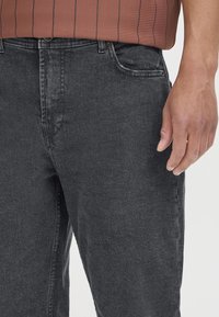 Temno sivi denim jeans s ravnim krojem, z sprednjimi žepi, zapiranjem na gumb in zadrgo ter rahlo zbledelostjo na tkanini.