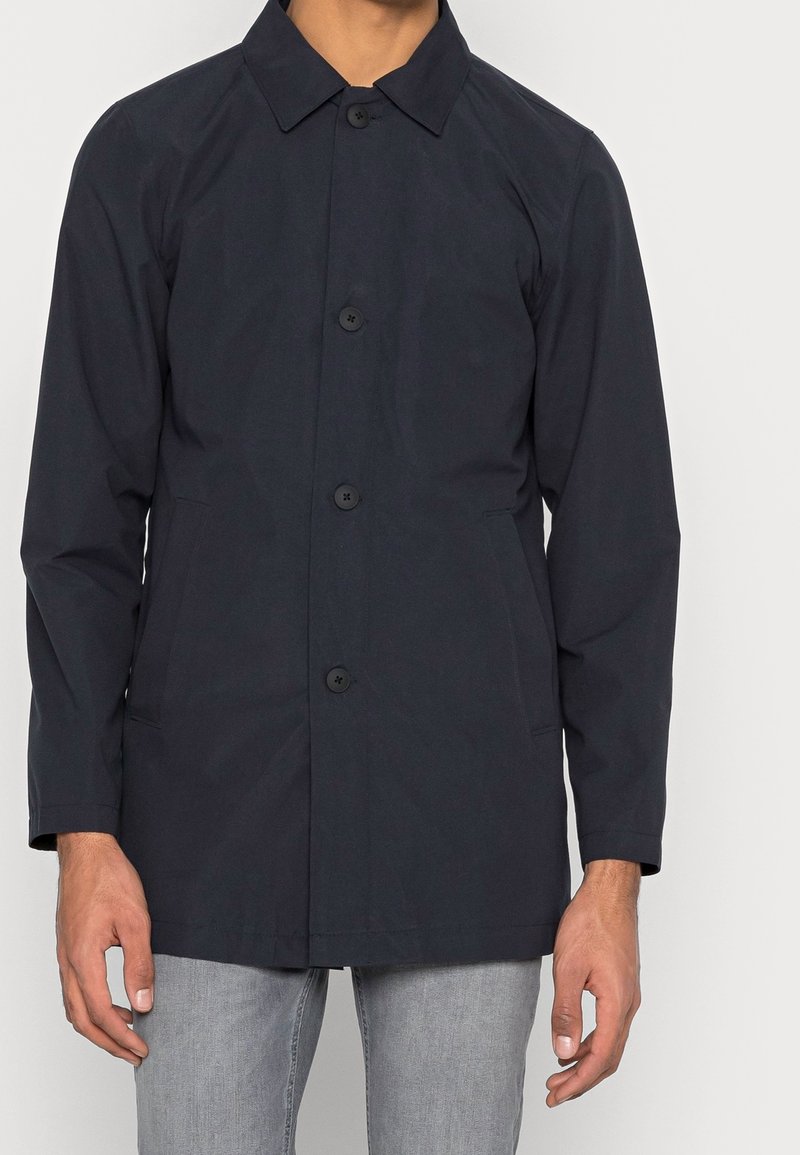 Marinblå lättviktsjacka med klassisk krage, framknäppning, två sidofickor och raglanärmar för en avslappnad passform.