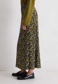 Zwarte rok met abstracte gele en witte patronen, textuurstof, vloerlengte, gecombineerd met zwarte loafers en een groene trui.