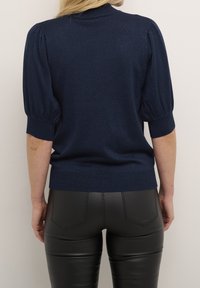 Marineblauwe gebreide pullover met opbollende korte mouwen en geribde manchetten. Soepele textuur met subtiele glans. Gecombineerd met strakke zwarte legging.