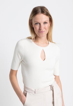 Weißes geripptes Strickoberteil mit einem Schlüssellochausschnitt und kurzen Ärmeln, kombiniert mit beigen hoch taillierten Hosen mit einem Gürtel.