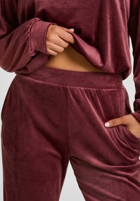 Bordeaux loungewear set gemaakt van zachte, pluche stof. Bevat lange mouwen, een aansluitende tailleband en zijzakken op de broek.