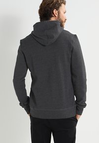 Mørkegrå hettegenser med myk, teksturert stoff. Har en romslig hette, ribbe-mansjetter og nede. Baksiden har et rent, minimalistisk design.