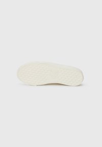 White sneaker sole with textured grip pattern, flat shape, rubber material, and embossed logo detail. Smooth surface, minimal design.