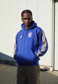 Felpa blu con strisce dorate sulle maniche, con emblema d'Italia. Realizzata in tessuto morbido, dotata di tasca a marsupio e cappuccio con cordino.