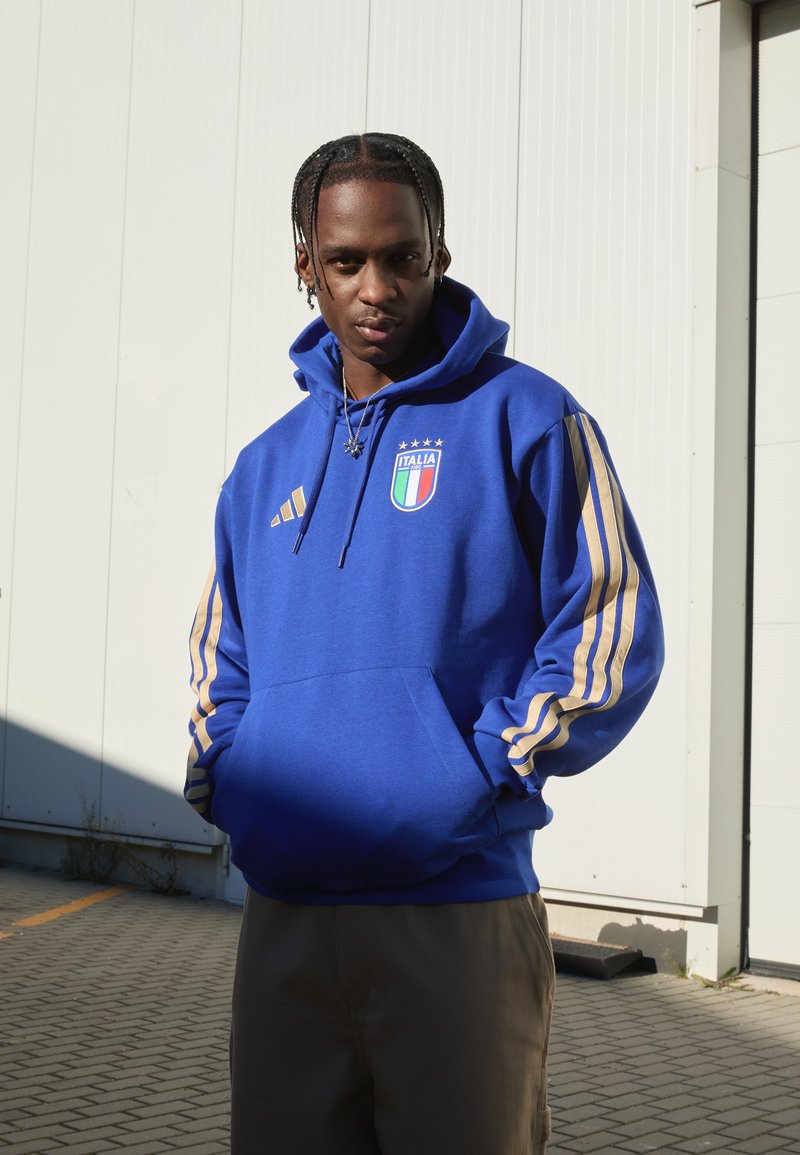 Felpa blu con strisce dorate sulle maniche, con emblema d'Italia. Realizzata in tessuto morbido, dotata di tasca a marsupio e cappuccio con cordino.