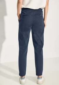 Marineblauwe broek met een zachte textuur, voorzien van een relaxed fit, achterzakken en een elastische tailleband, gecombineerd met witte sneakers.