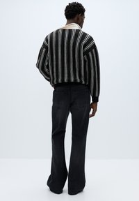 Maglione a righe bianche e nere con silhouette ampia, abbinato a jeans scuri a zampa, visto da dietro su uno sfondo chiaro.