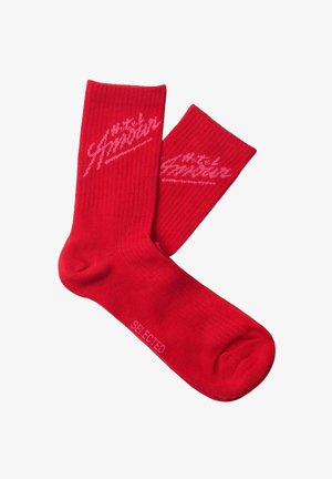 Pereche de șosete roșii cu manșete tip coardă, având un logo script roz lângă vârf și textul „SELECTED” pe talpă.