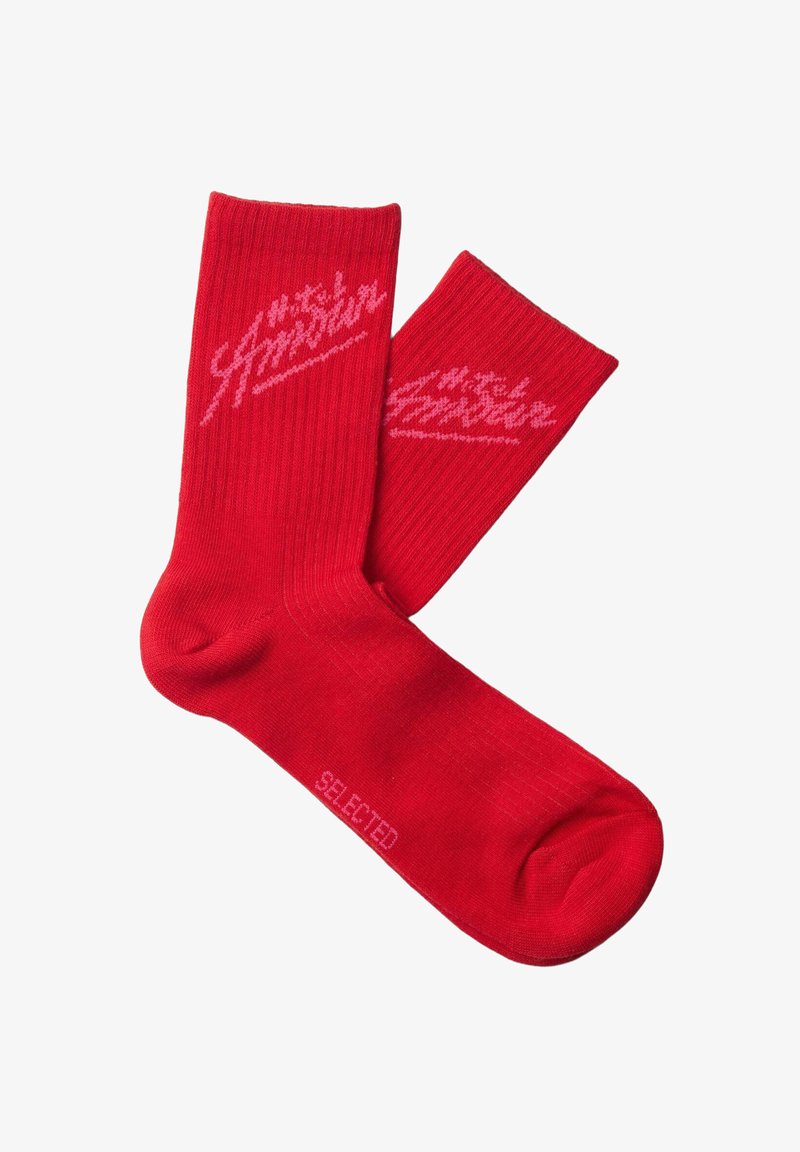 Paire de chaussettes rouges à bord-côtes, avec un logo en écriture rose près du haut et le mot "SELECTED" inscrit sur la semelle.