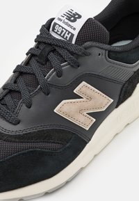 Baskets noires et grises, avec une tige texturée, des détails en mesh et un logo en suède beige proéminent. Semelle intermédiaire blanche avec marquage.