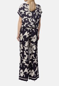 Gemusterter Jumpsuit mit floralen Motiven in Marineblau und Cremé, mit kurzen Ärmeln, lockerer Passform und weit geschnittenen Hosen mit einer gebundenen Taillendetail.